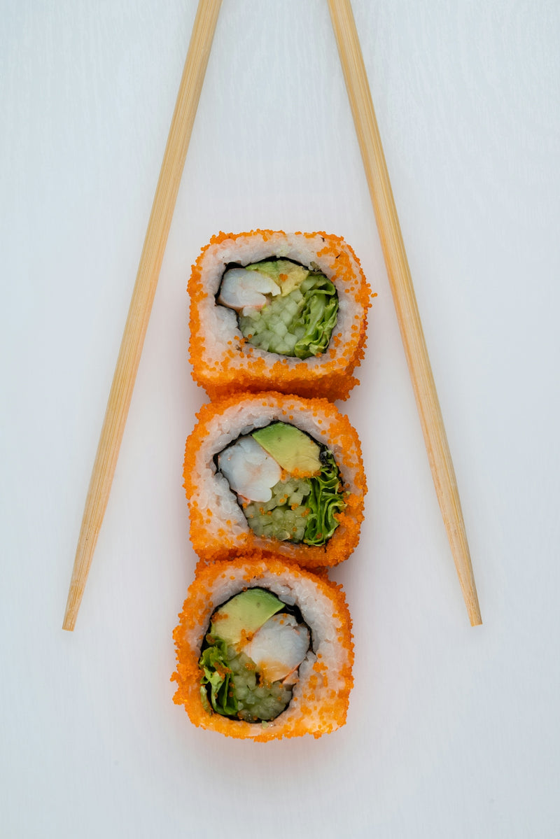 Three sushi rolls on a white surface with chopsticks