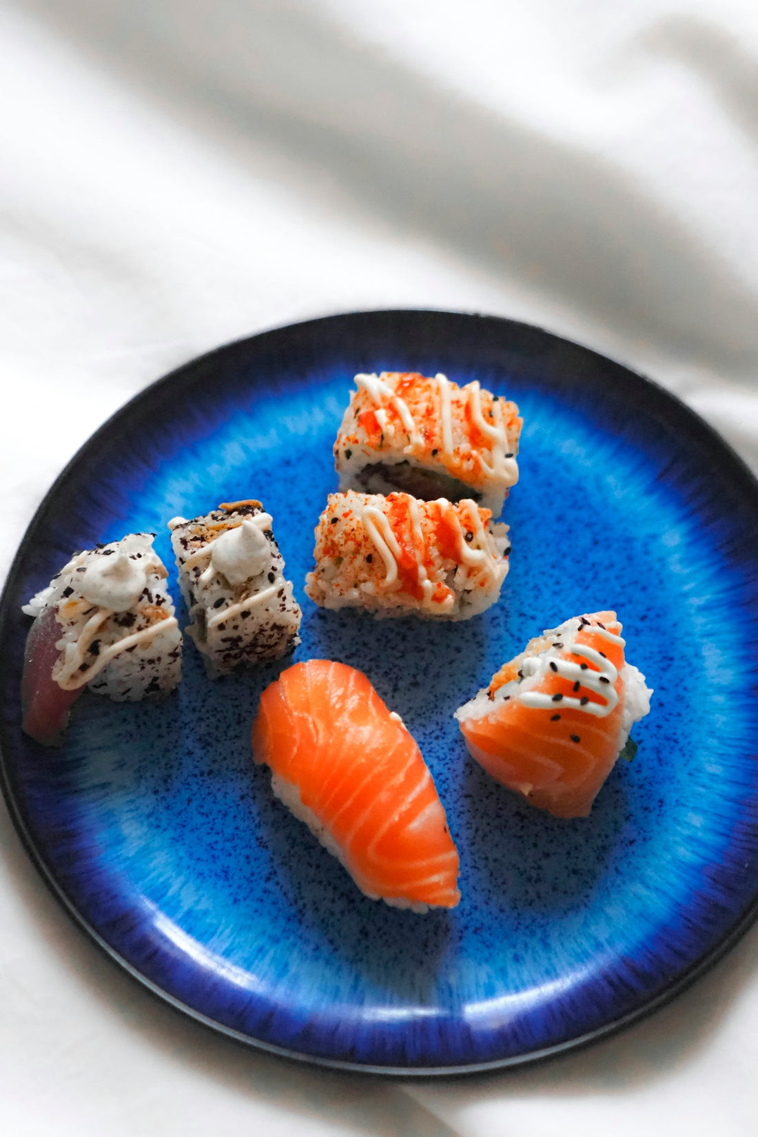 A blue plate topped with sushi on top of a bed