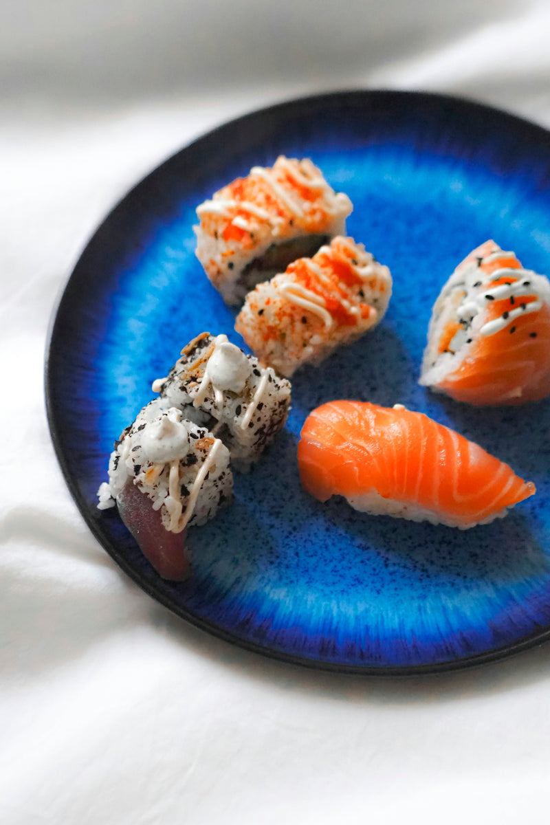 A blue plate topped with sushi on top of a white table