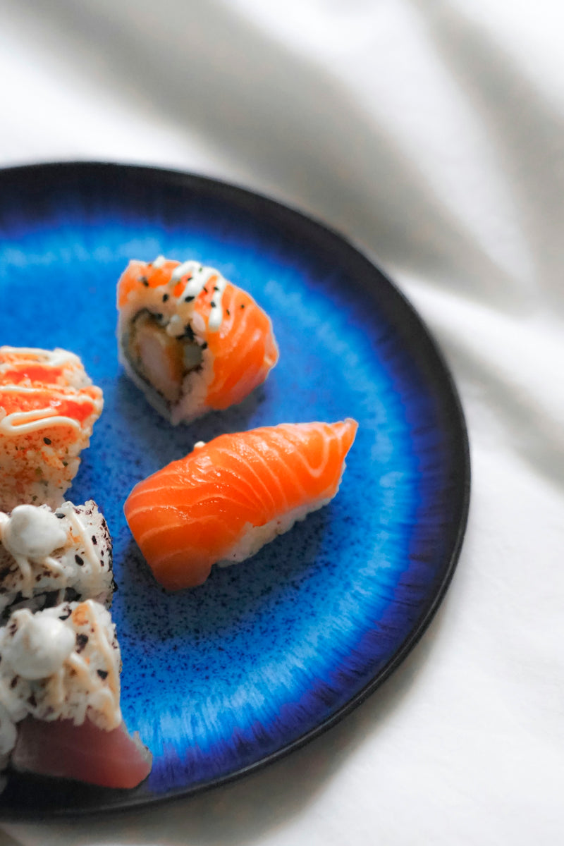 A blue plate topped with sushi on top of a white table