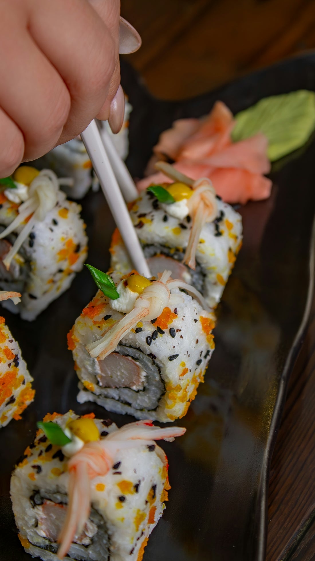 A person eating sushi with chopsticks on a black plate