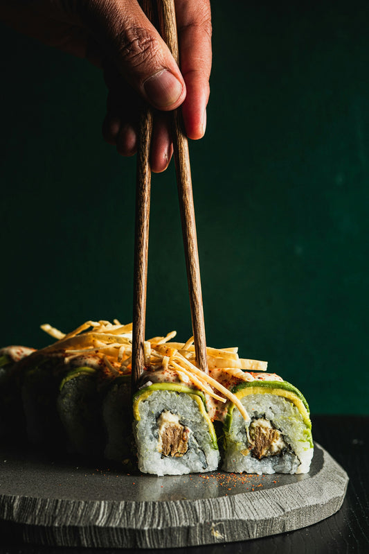 Chopsticks picking up avocado sushi roll with crispy topping.
